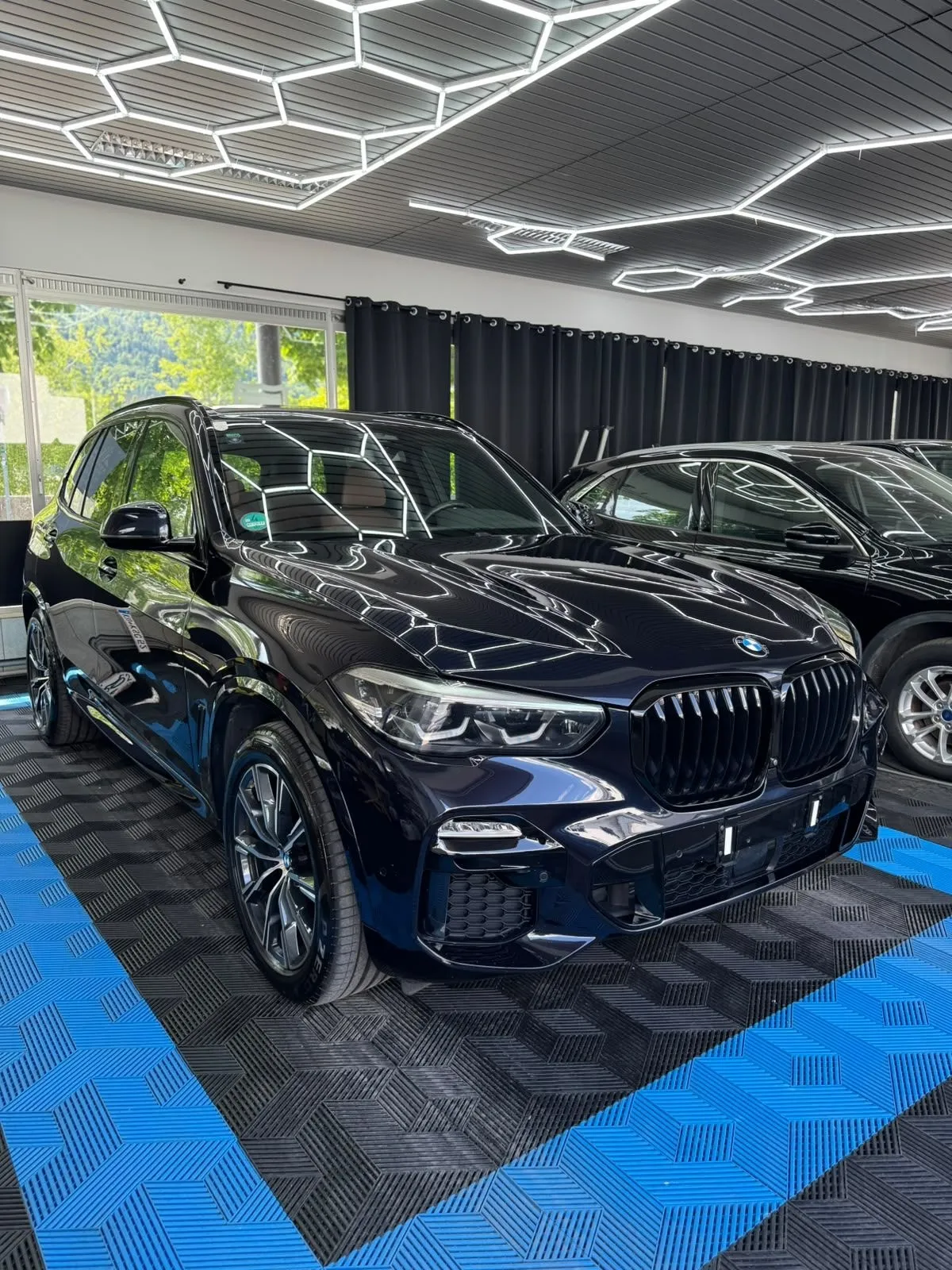 BMW X5 in der Halle von Saff Car Lounge in Kufstein nach der Aufbereitung, Hexagon-Leuchten spiegeln sich im Lack