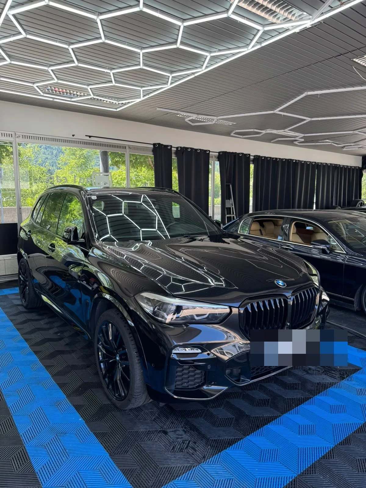 BMW X5 in der Halle von Saff Car Lounge in Kufstein nach der Aufbereitung, Hexagon-Leuchten spiegeln sich im Lack