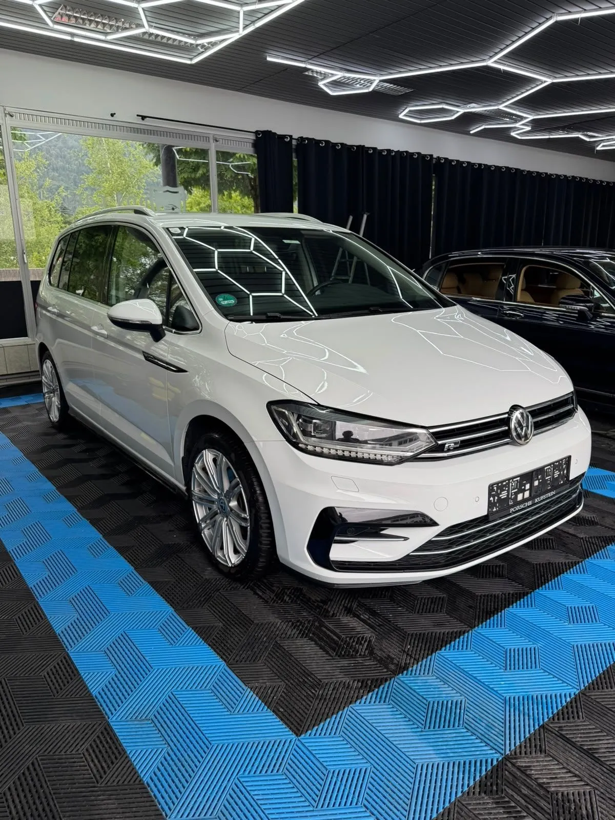 VW Touran in der Halle von Saff Car Lounge in Kufstein nach der Aufbereitung, Hexagon-Leuchten spiegeln sich im Lack